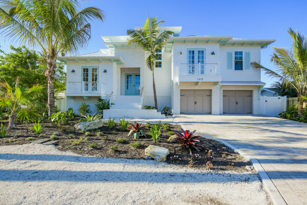 Eason Builders custom home on a FL Barrier Island. white house with two balconies, double garage, landscaped front yard, palm trees, and a gravel driveway.